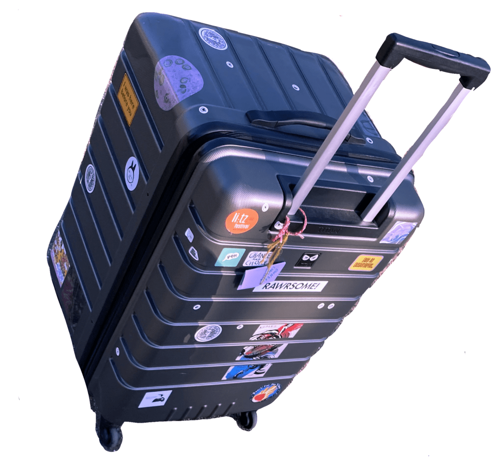 Riesiger Koffer, in dem Lui ihre Zines transportiert. Auf dem Koffer sind viele bunte Sticker von Festivals und anderen Zinemacher*innen und Künstler*innen aufgeklebt.